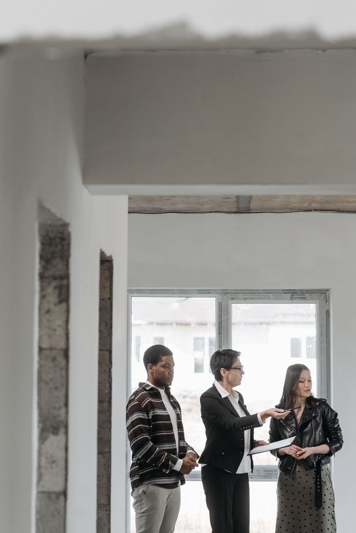 Real estate agent showing a house to diverse clients indoors, discussing property details.